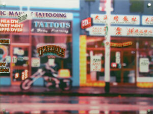 Artwork of a tattooist and newspaper shop fronts, highlighting all of the shop signage and street signs